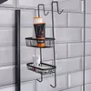 A black metal shower caddy with two shelves, holding toiletries and a bar of soap, hanging on a shower door. The background is white subway tiles. Náhled obrázku produktu