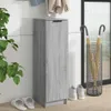 A tall, narrow gray wood-effect cabinet with a handle on top, placed against a white wall. There are coats hanging on a rack above the cabinet. To the right, there is an umbrella stand with two yellow umbrellas. Two pairs of slippers are on the floor in fr Podgląd zdjęcia produktu
