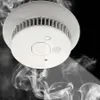 A white smoke detector is shown against a black background with wisps of smoke rising from below. Voir les images du produit