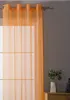 An orange sheer curtain hangs in front of a window, with a small plant in a vase on a wooden surface to the right. Produktbild-Vorschau