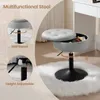 A multifunctional stool with storage is shown on a fluffy white rug next to a vanity table. Produktbild-Vorschau