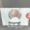 Hands are shown tying a white trash bag with red ties inside a silver trash can. Produktbild-Vorschau