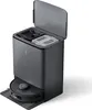 A dark gray robot vacuum cleaner docked in its charging and self-emptying station, with the station's lid open revealing compartments for dust and water. Produktbild-Vorschau
