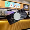 A smartphone with a magnetic charging puck attached, suspended in front of a cafe counter with menu boards in the background. Anteprima dell’immagine prodotto