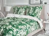 A bed with green leaf patterned bedding and white pillows in a bedroom setting. Náhľad obrázku produktu