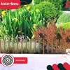 A garden scene with a wooden fence in the foreground and various plants and flowers in the background. Produktbild-Vorschau