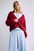 A woman is modeling a red cardigan over a light blue top and light blue pleated pants. Produktbild-Vorschau