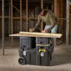 A man is measuring a piece of wood on top of a stack of toolboxes. Anteprima dell’immagine prodotto