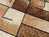 A close-up view of a rectangular rug with a geometric pattern in shades of beige, brown, and black. Náhled obrázku produktu