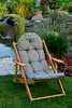 A wooden deck chair with a gray cushion is placed on a green lawn in front of a garden pond with a waterfall and lush vegetation. Anteprima dell’immagine prodotto