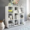 A white cube bookshelf filled with various decorative items and storage boxes, set against a gray wall. Produktbild-Vorschau