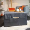 A grey ottoman with pockets is shown in a living room setting, with a tablet and tray on top. Voir les images du produit