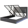 A dark gray upholstered bed frame with its hydraulic lift mechanism open, revealing the slatted base and storage space underneath. Blue LED lighting is visible along the bottom edge of the frame. Náhled obrázku produktu