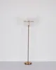 A floor lamp with a metallic gold finish and a ribbed glass shade stands against a plain white wall. Náhľad obrázku produktu
