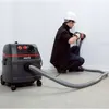 A person wearing a hard hat and safety glasses is using a Starmix industrial vacuum cleaner while drilling into a wall. Produktbild-Vorschau