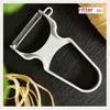 A white peeler is placed on a dark surface, with some potato peels in the foreground and a logo in the top right corner. Voir les images du produit