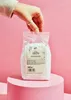 A hand holding a bag of salt over a pink pedestal. Produktbild-Vorschau