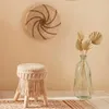 A bohemian-style room with a macrame stool, a woven wall hanging, and a glass vase with dried palm leaves. Anteprima dell’immagine prodotto