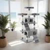 A multi-level cat tree with enclosed spaces and platforms, placed near a window with a view of the ocean and beach. Two cats are visible on the cat tree. Voir les images du produit