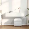 A white floating shelf with two drawers mounted on a white wall above a white ottoman. Náhled obrázku produktu
