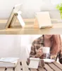 The image shows two scenes. The top scene displays two white tablet stands on a wooden surface. The bottom scene shows a woman holding a cup of coffee while sitting at a table with a book and a tablet stand holding a phone. Náhľad obrázku produktu