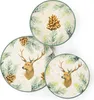 A set of three round plates with a winter-themed design featuring deer, pine branches, and pinecones. Podgląd zdjęcia produktu
