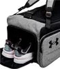 A close-up view of a grey Under Armour duffel bag with a shoe compartment open, revealing a pair of black and white sneakers. Náhled obrázku produktu