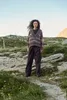A woman stands on a rocky, grassy hillside with a clear sky in the background. Produktbild-Vorschau