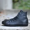 A pair of black leather Converse Chuck Taylor high-top sneakers are placed on a concrete surface. Produktbild-Vorschau