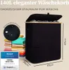 A black laundry basket with a wooden lid is shown, with a stack of colorful folded clothes next to it. A close-up of the fabric shows water droplets, indicating it is water-repellent. Dimensions are indicated. Produktbild-Vorschau