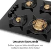 A close-up, angled shot of a black gas stovetop with four burners. The burners have brass flame diffusers and black grates. The stovetop has a glossy finish. Text in French is overlayed at the bottom. Podgląd zdjęcia produktu