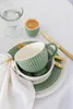 A table setting with a green mug and saucer, plates, and cutlery. Produktbild-Vorschau