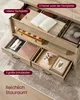 Interior view of a wooden coffee table with open drawers and compartments, showcasing storage space and items like books, a game controller, and a framed picture. Produktbild-Vorschau