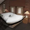 A large, plush white duvet or mattress topper is displayed on a bed in a bedroom setting with brick walls and bedside lamps. Produktbild-Vorschau