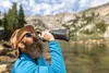A man drinking from a collapsible water bottle by a lake in a mountainous area. Produktbild-Vorschau