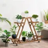 A wooden plant stand with multiple tiers filled with various potted plants, set against a white wall. Produktbild-Vorschau