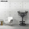 A modern gym or home fitness setup with a MAXXUS back trainer, a white armchair, and a small gold side table against a concrete wall. Produktbild-Vorschau
