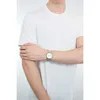A person wearing a white t-shirt and a silver watch on their left wrist. Voir les images du produit