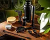 A collection of barware tools arranged on a wooden surface with a tiled background. Voir les images du produit