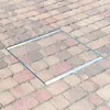 A square metal frame is set into a paved surface made of rectangular bricks. Produktbild-Vorschau
