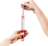 Two hands are holding a glass cylinder filled with pink liquid, and a thermometer is being inserted into it. Produktbild-Vorschau