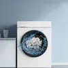 A washing machine with filter balls and water splashing inside the drum, next to a cabinet with a soap dispenser. Produktbild-Vorschau