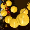 A string of yellow paper lanterns illuminated by internal lights, hanging in a dimly lit environment, possibly outdoors or near a Christmas tree. Produktbild-Vorschau