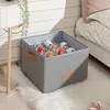 A grey fabric shoe organizer with multiple compartments filled with shoes, placed on a fluffy white rug next to a bed and a desk. Náhled obrázku produktu
