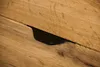 A close-up shot of a black drawer pull on a wooden drawer. Produktbild-Vorschau