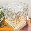 A hand holding a cube-shaped lamp with a textured glass shade and a wooden base. Produktbild-Vorschau