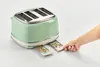 A green vintage-style toaster with two crumb trays pulled out, and a hand reaching to pull out one of the crumb trays. Produktbild-Vorschau