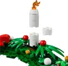 A close-up view of a LEGO® Seasonal wreath build, featuring green foliage, red berries, and white candle-like structures topped with a golden flame. Podgląd zdjęcia produktu