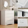 A white dresser with four drawers is shown in a bedroom setting, next to a bed with green pillows. The right side of the image displays close-ups of product features with German text labels. Náhled obrázku produktu