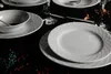 A table setting with white porcelain plates and bowls, decorated with a subtle geometric pattern, set against a dark background. Náhľad obrázku produktu